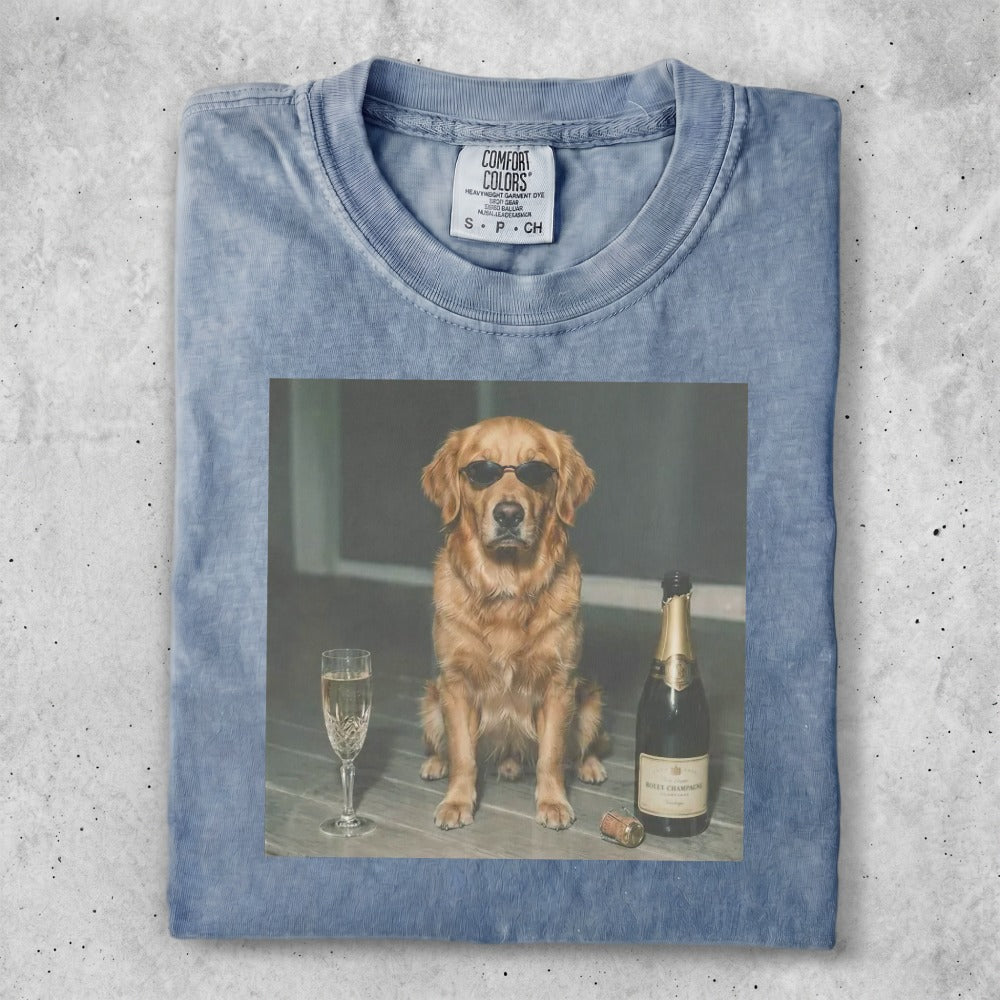 Golden retriever wearing sunglasses sits next to champagne and a glass.