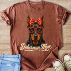Brown t-shirt with Doberman wearing heart glasses and a red polka dot bow.