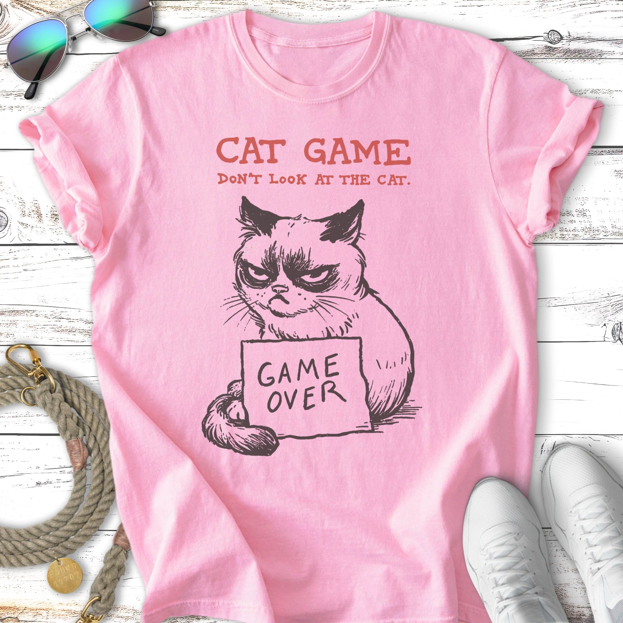 Pink t-shirt with grumpy cat graphic and text "CAT GAME DON'T LOOK AT THE CAT. GAME OVER."