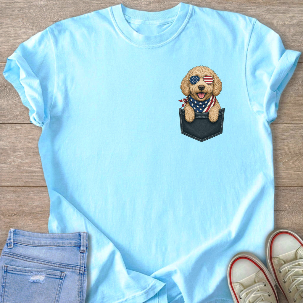 Light blue t-shirt with a golden doodle wearing American flag sunglasses and bandana in a pocket.
