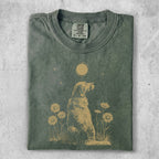 Golden retriever sitting in grass with sunflowers and moon design on green t-shirt.