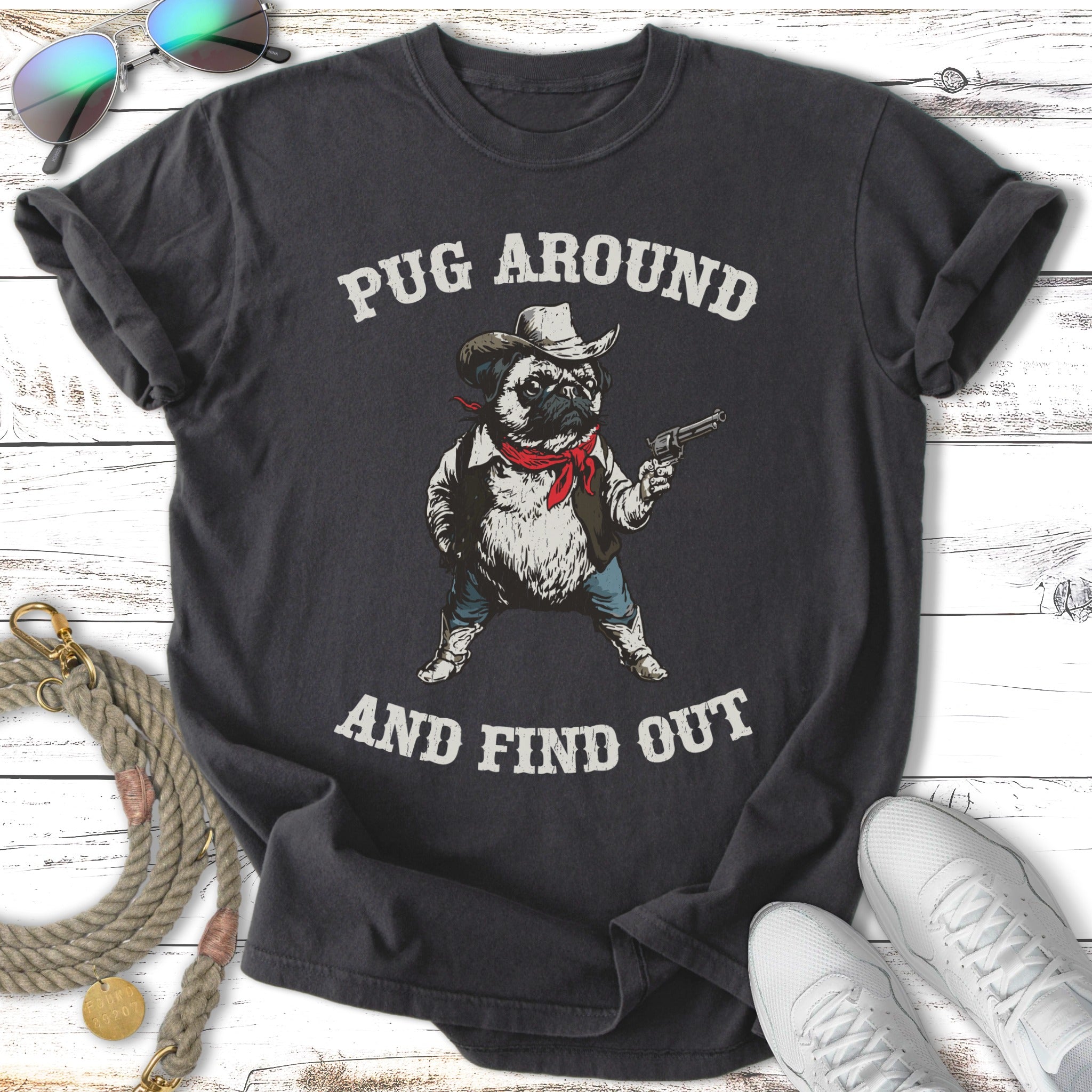 Dark t-shirt with a cartoon pug wearing a cowboy hat and holding a gun, text reads "PUG AROUND AND FIND OUT".