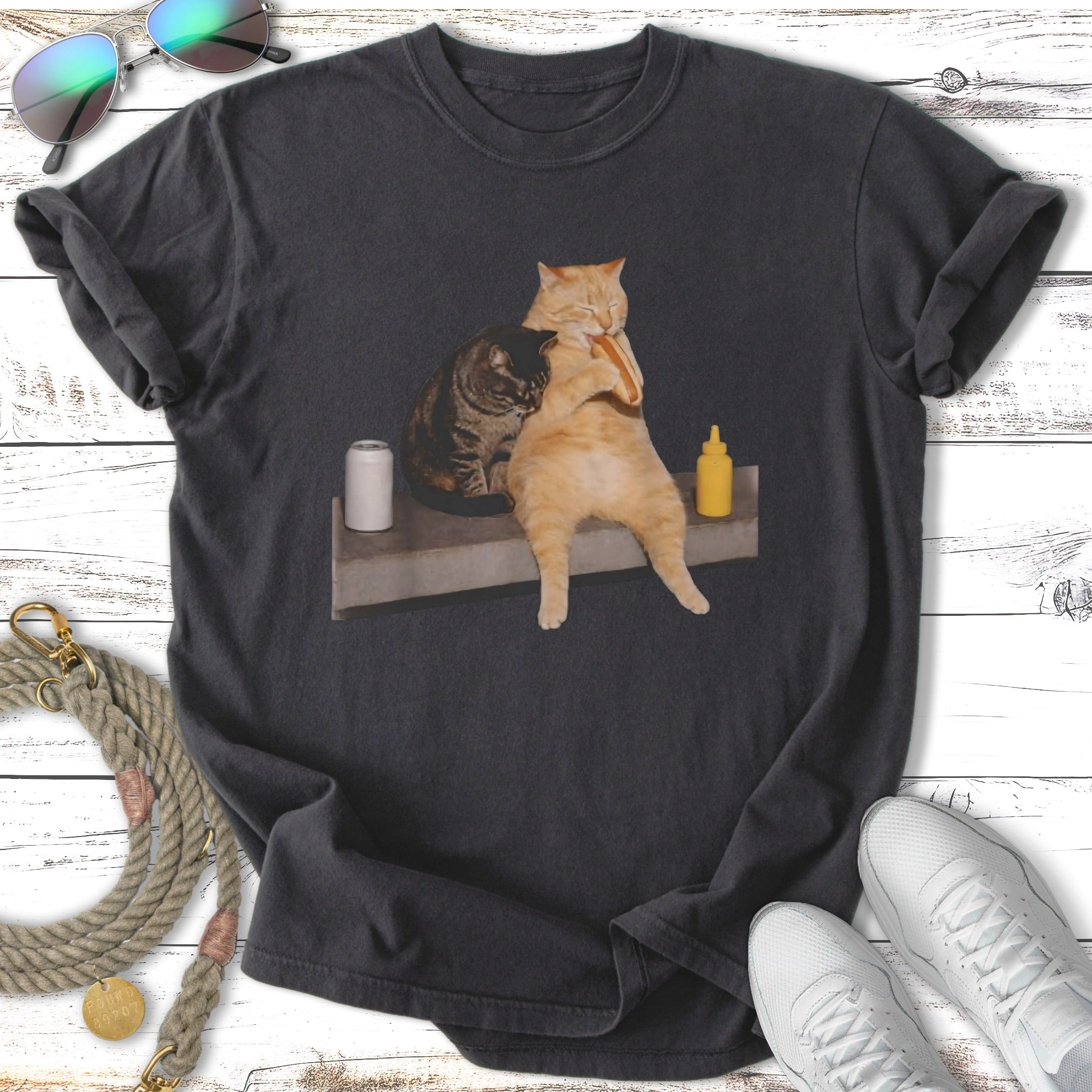 Two cats, one with a hot dog in its mouth, sit on a ledge.